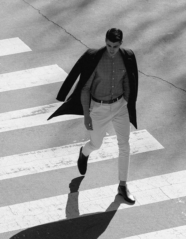 Hombre joven andando por un paso de peatones con ropa ecológica y chaqueta